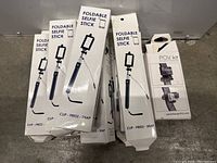 Multiple boxed foldable selfie sticks stacked vertically, showing front product packaging with image and text.