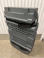 Side angled view of the vertically standing gray plastic trade show case showing molded handles, securing straps, and reinforced texture.