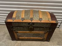 Front view of vintage dome top steamer trunk chest showing wood slats, metal sheeting, latch and leather corner coverings.