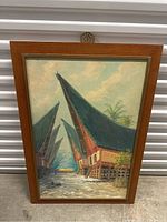 Front view of a framed vintage oil painting depicting stilt houses with tall peaked roofs and a waterway.