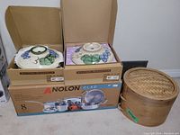 Two ceramic tureens with lids in boxes and bamboo steamer basket beside an Anolon Clad cookware box