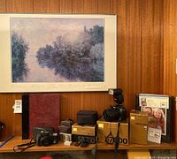 Overall display of framed Monet poster above cameras, cases and albums on wooden shelf