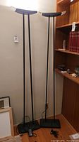 Two tall, slim black floor lamps standing side by side, showing height and base design.