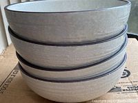 Stack of four light beige ceramic bowls with crackle glaze and dark rims.