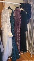 Wide view of the white wedding dress and three evening gowns on a clothing rack with the fur coat hung behind them.
