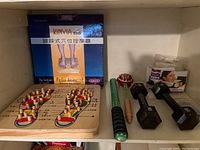 Photo showing Kinyia Pedal Acupoint massage board with wooden knobs, two massage rollers, two black hex dumbbells, and forehead band on shelf.