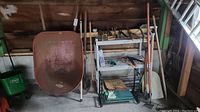 Overview of wheelbarrow, long-handled tools, spreader and small hand tools on metal shelf