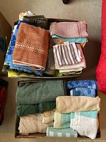Two cardboard boxes filled with assorted towels in multiple colors and sizes placed on the floor.