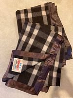 Two folded checkered chocolate brown wool blankets with satin trim shown on neutral surface, one with label 'Night Queen 100% wool Made in India'.