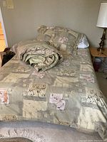 Full view of the bed made with beige patterned comforter and pillows, green comforter folded on top.
