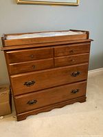 Front view of wooden change table dresser with drawers and raised sides for changing pad.