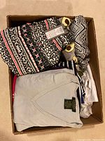 Box filled with various women's knitwear including folded sweaters with patterns and solid colors, tags visible on some items indicating new condition, mostly in small to medium sizes.