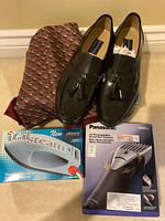Photo of Bostonian shoes, men's scarf, Panasonic rechargeable beard/hair trimmer, and ItalaSteam travel iron in their boxes arranged on a beige carpet.