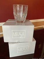 Two light gray Mikasa branded boxes stacked, one open showing a crystal whiskey glass on top, clear crystal with vertical cuts.