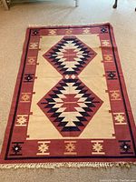 Full view of the Navaho inspired woven rug laid on carpet floor showing overall design and fringed edges.