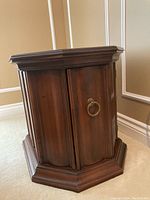 Front view of octagon shaped solid wood side table, showing hinged door and brass-tone ring pull handle