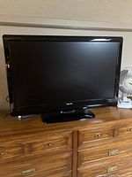 Front view of Phillips 42 inch black flat screen TV placed on wooden dresser, powered off, with remote control visible in reflection or adjacent.