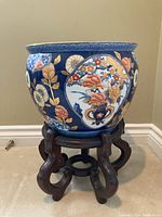 Side view of ceramic planter on wooden stand, showing floral design and shape.
