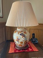 Full view of one ceramic lamp showing floral pattern on base and pleated cream lampshade