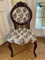 Front view of one chair showing dark wood frame, button-tufted floral tapestry upholstery on seat and back, and curved legs.