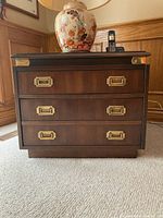 Front view of wood side table with three drawers and brass hardware, showing overall condition and style.