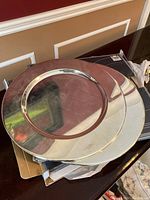 Stacked silver charger plates with reflective surfaces, showing round shape with a decorative inner indentation.