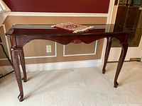 Front view of a dark wooden sofa table with French provincial style legs, placed against a red wall with white molding and beige carpet.