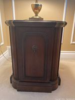 Side view of solid wood side table with fluted vertical details, decorative keyhole on front door, and raised base.