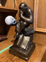 Full view of bronze sculpture depicting a pensive ape holding a white skull, seated on books including one inscribed "Darwin."