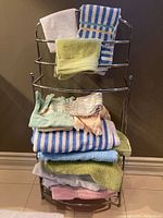Chrome towel rack holding various folded towels in blue, green, pink, white, and patterns including stripes and lace trim