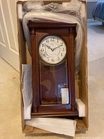 ERGO wall clock in original packaging, showing wooden frame, clock face with Arabic numerals, and protective foam around clock inside box.
