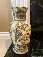 Photo of the West German pottery vase showing the raised floral design and scalloped top edge, placed indoors on carpeted floor against a wall.