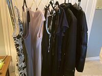 Photo of seven women's dresses and jackets hanging on a horizontal bar, showing assortment of light pink, black, and patterned dresses and jackets in black.