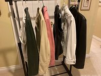 Five women's leather jackets in various colors and one pair of off-white pants hanging on a garment rack.