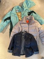 Three women's jackets laid out on carpet showing full front view including Columbia mint green jacket with detachable hood at top, Joe Fresh medium green jacket in middle, and Jessica denim jacket at bottom.