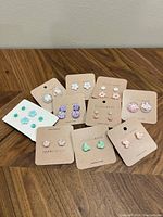 Ten sets of assorted resin stud earrings displayed on branded cardboard cards, showing various colors and designs including flowers, geometric, and iridescent styles.