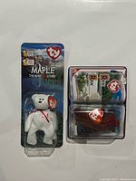 Front view of Maple The Bear Beanie Baby sealed on blue card backing and Rex The Tyrannosaurus Rex sealed with fold-out card, all sealed in original plastic clamshell cases.