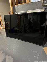 Front view of large flat screen TV with black frame, turned off, showing a reflective dark screen.