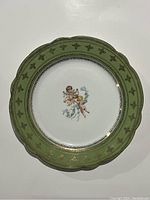 Top view of Carlsbad decorative plate showing central cherub design, green and gold detailed border with scalloped edges.