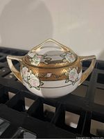 Front angled view of the antique Nippon sugar bowl showing the floral handpainted design, gold detailing, lid with triangular handle and two side handles.