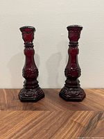 Front view showing two dark red Avon Cape Cod glass candlesticks with hexagonal bases and ornate embossed detail
