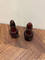 Pair of ruby red cranberry glass salt and pepper shakers with geometric faceted design and heart motif, standing upright on a wooden surface against a plain wall.