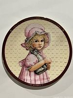 Front of the limited edition Jan Hagara plate depicting a young girl in a pink bonnet and dress holding a kitten, marked 1984.