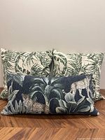 Three decorative throw pillows shown together, two with green palm leaf print and one with dark blue cheetah design