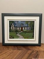 Framed painting depicting a cottage with greenery, pathway, and flowers