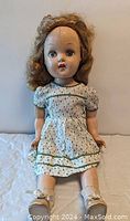 Full front view of vintage 1940's plastic doll seated, showing dress and shoes