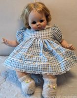 Front view of vintage Madame Alexander doll wearing blue gingham dress and knit booties, showing cloth body and facial features with sleepy eyes.