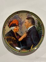 Front view of the Norman Rockwell "Love's Reward" plate showing artwork of a woman pinning a flower on a man's lapel with colorful decorative border.