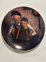 Front view of the Norman Rockwell "The Music Maker" plate showing an elderly man and a boy playing accordion in warm colors with artist's name in red.