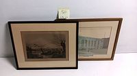 Two framed lithograph prints shown leaning against a wall, one with architectural subject and the other hunting scene.